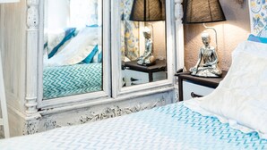 A bedroom with a large white cabinet, a bed with patterned bedding, a small table with a lamp, and a wall with burlap sacks.