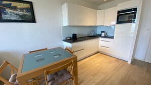 Une cuisine de taille réduite avec des meubles blancs, un four noir et une table à manger avec des chaises.