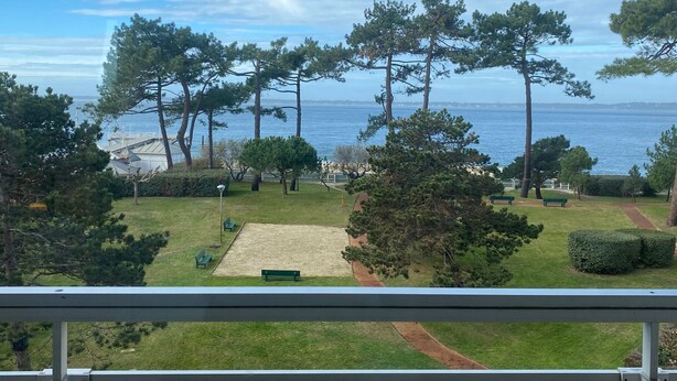 Une vue depuis un balcon donnant sur un parc avec des bancs, une zone sablonneuse et une étendue d’eau.