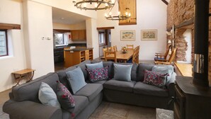 A modern living room with a sectional sofa, a fireplace, and a dining area with wooden furniture. - Spacious Converted Barn on a Flower Farm, Devon Countryside, Family Friendly (Kentisbeare)