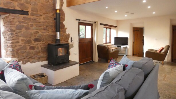 A cozy living room with a stone wall, a fireplace, a television, and comfortable seating. - Spacious Converted Barn on a Flower Farm, Devon Countryside, Family Friendly (Kentisbeare)