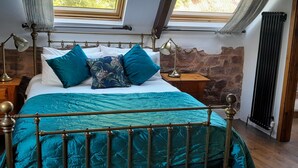 A bedroom with a bed, two bedside lamps, a stone wall, and a window with curtains. - Spacious Converted Barn on a Flower Farm, Devon Countryside, Family Friendly (Kentisbeare)