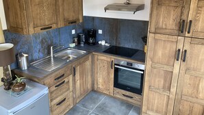 Una cocina compacta con armarios de madera, un lavamanos de acero inoxidable, un horno empotrado y una cafetera.