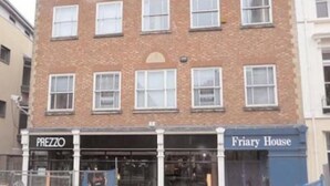 A multi-story building with a brick facade and multiple windows. The ground floor has a storefront with signs reading "PREZZO" and "Friary House." - Friary House Serviced Apartments by Roomsbooked - 24Hr Reception (Gloucester)