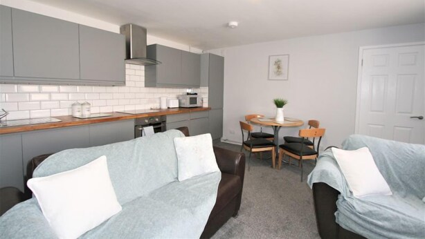 A compact living space with a kitchenette, two sofas, a dining table, and a small garden view. - Friary House Serviced Apartments by Roomsbooked - 24Hr Reception (Gloucester)