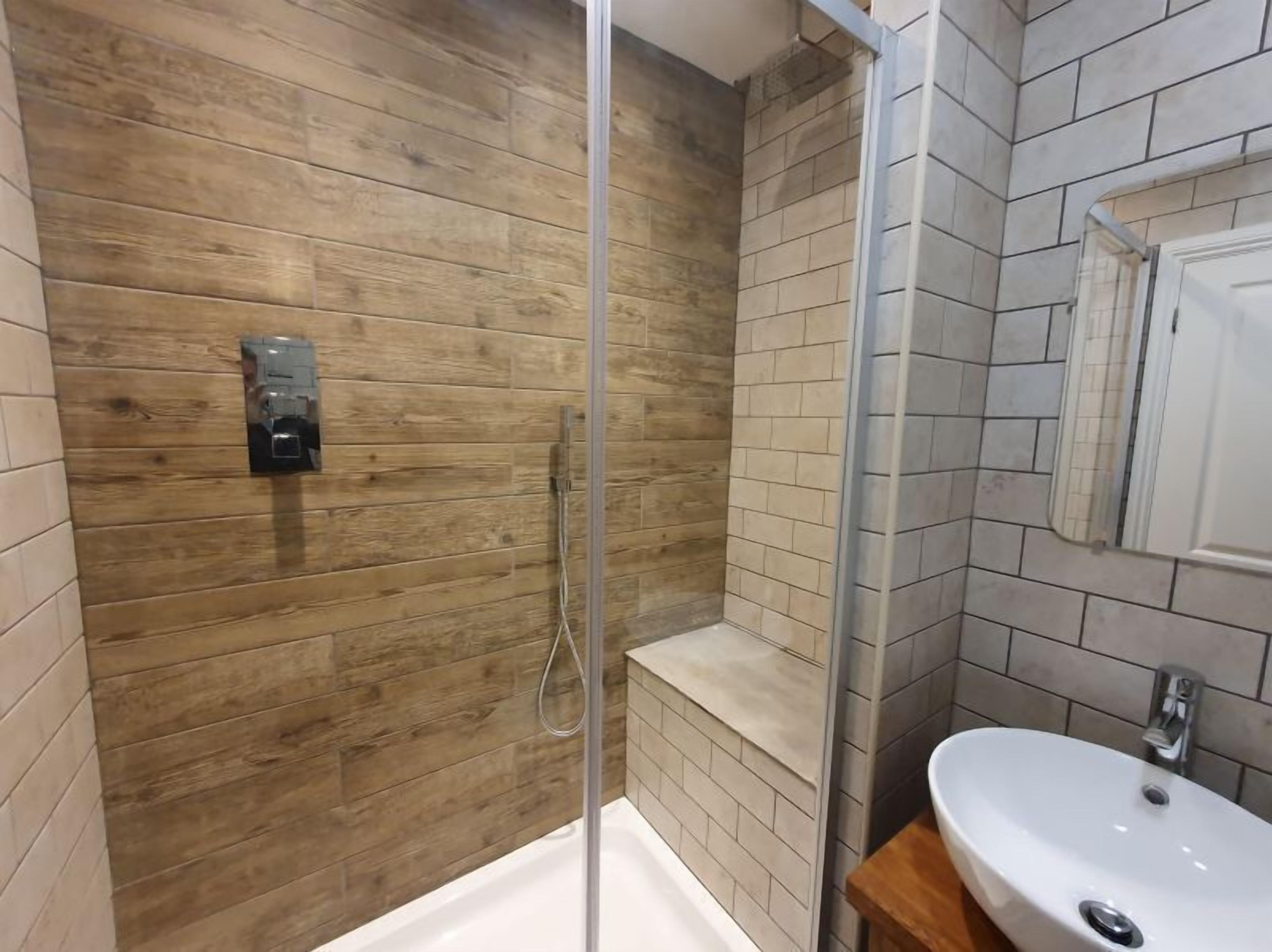 Un baño moderno con pared de madera, mampara de ducha de vidrio y lavamanos blanco con espejo.
