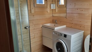 Ein kleines Badezimmer mit Holzwänden, einem Waschbecken, einer Waschmaschine und einer Toilette.