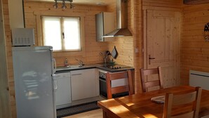 Eine kleine Küche mit Kühlschrank, Herd, Spüle und Holzkästen um einen Tisch.
