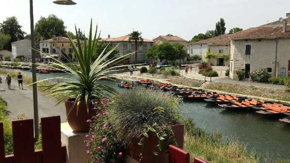 A riverside view with boats, a potted plant, and traditional buildings. - CHARMING GITE IN THE MARAIS POITEVIN (Magné)
