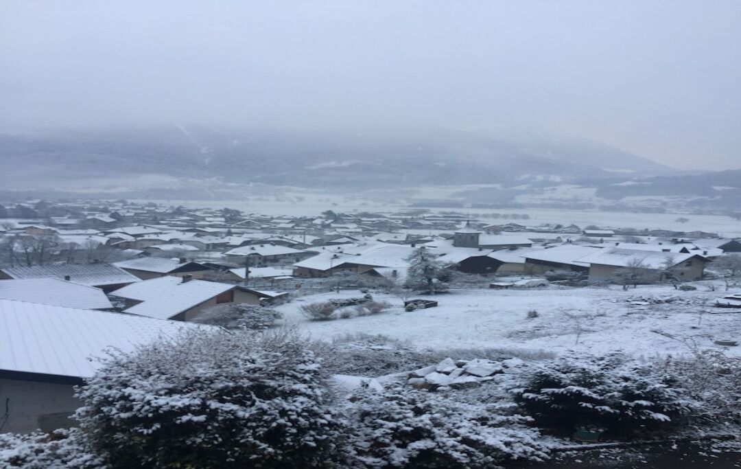 Ein verschneites Dorf mit mehreren Häusern, von denen einige schneebedeckte Dächer haben, und einigen Gebäuden im Hintergrund.