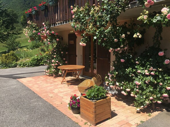 A wooden outdoor seating area with a table and chairs, surrounded by potted plants and blooming roses.
