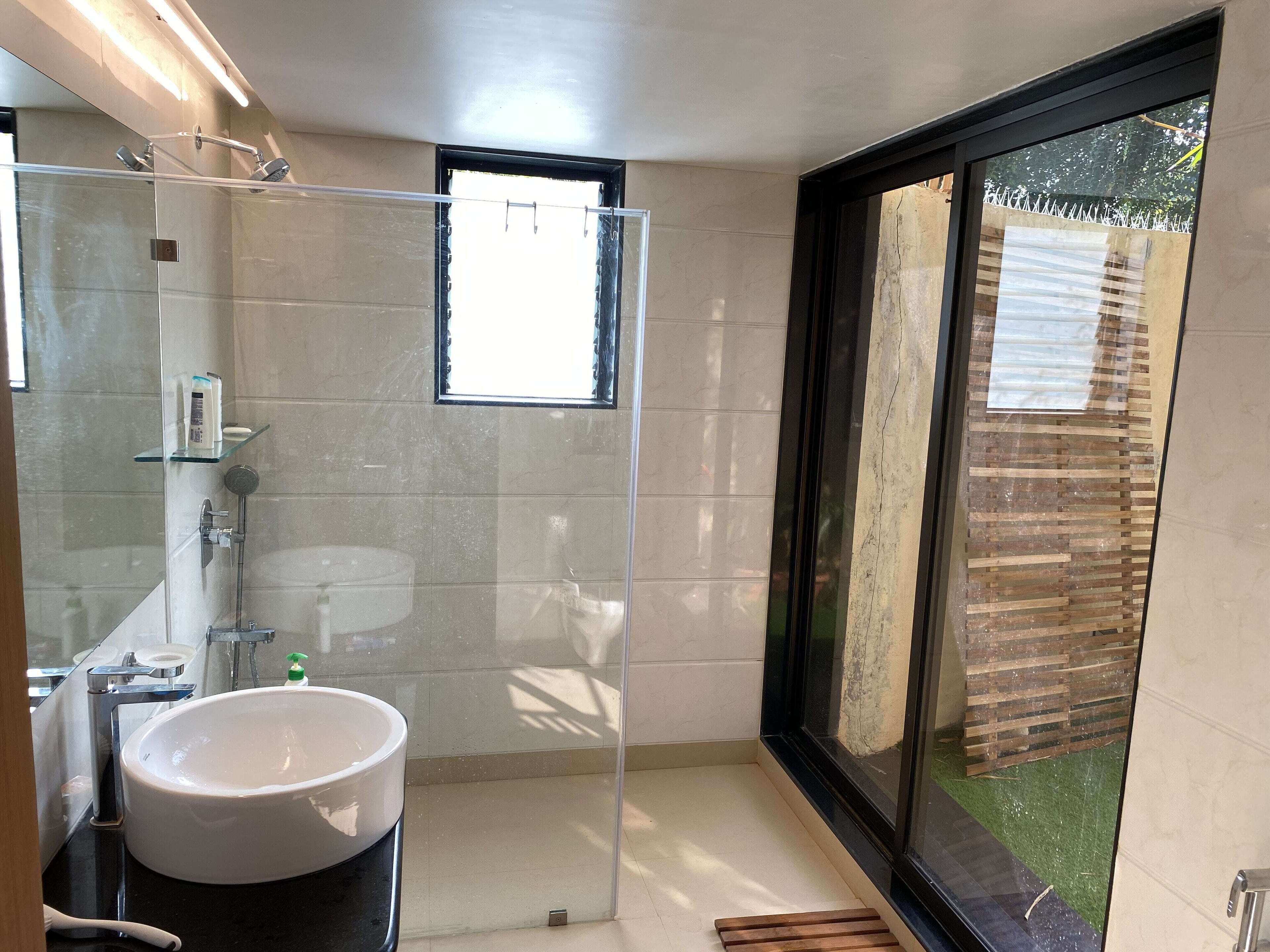 Un bagno moderno con box doccia in vetro, lavandino bianco e un'ampia finestra che offre vista sull'esterno.