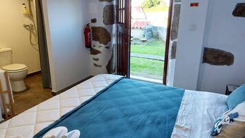Habitación de hotel con cama, baño con ducha, inodoro y extintor.