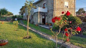Un edificio in pietra con un giardino antistante, che include un piccolo albero e piante in vaso.