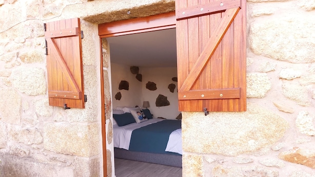 Un edificio in pietra con una porta in legno che conduce a una camera da letto con un letto, cuscini e una lampada a muro.