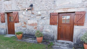 Un edificio in pietra con porte e persiane in legno, piante in vaso e un vialetto in pietra ciottolata.