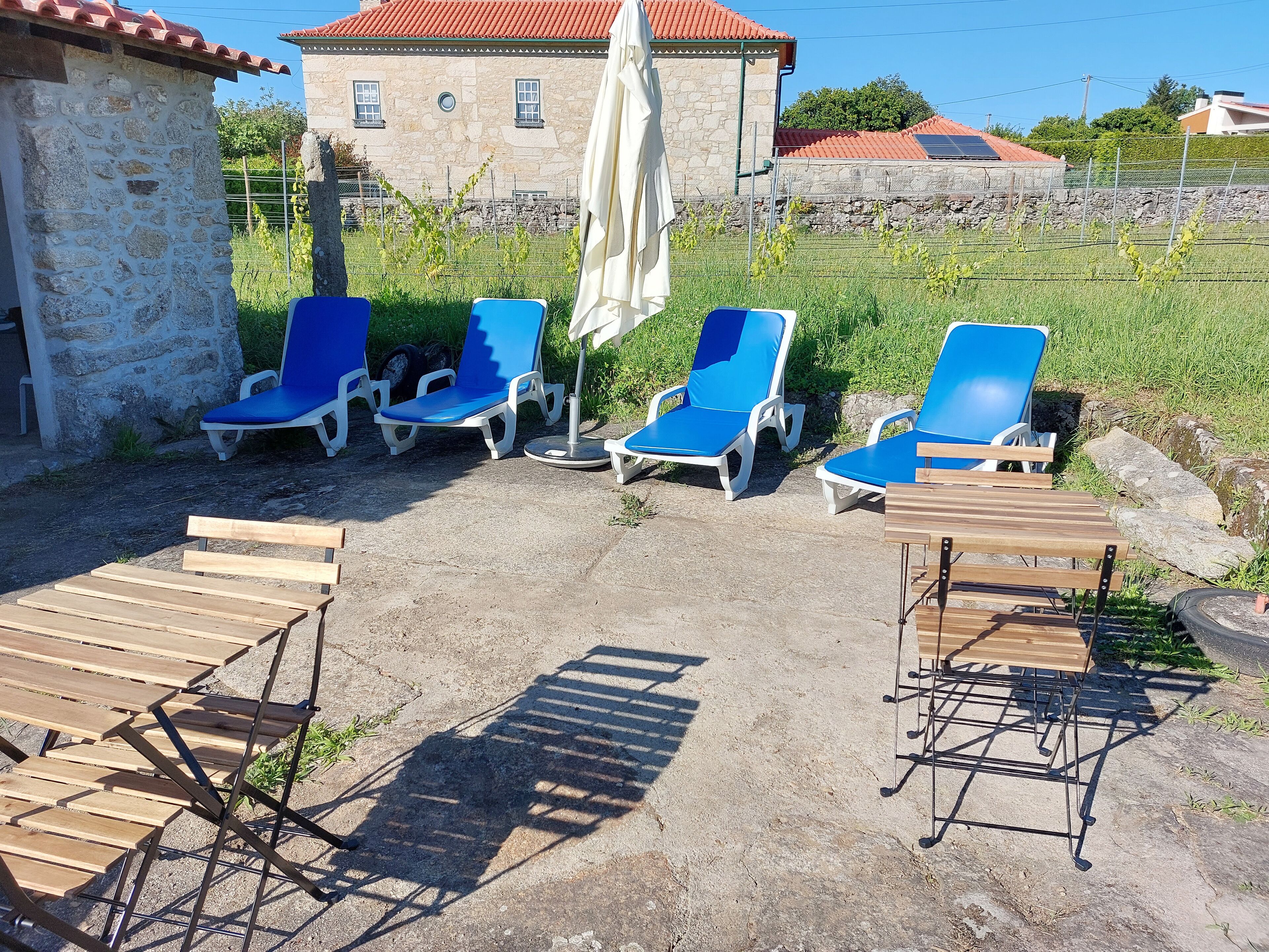 Outdoor seating with blue lounge chairs and wooden tables, a stone building in the background, and a clear sky.