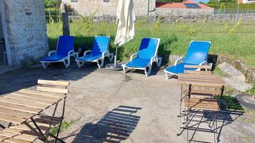 Outdoor seating with blue lounge chairs and wooden tables, a stone building in the background, and a clear sky.