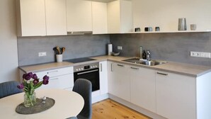 A modern kitchen with white cabinets, a built-in oven, and a sink. There is a vase with flowers on the table.