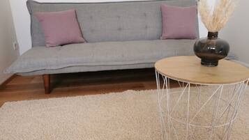 En grå sofa med to puder, et rundt træsofabord med metalstel og en beige, luvrigt måtte.