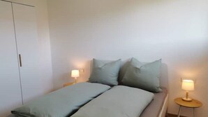 A single-bed room with a wooden floor, a white wardrobe, and two bedside lamps.
