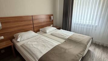 Ein Doppelbett mit Holz-Kopfteil, zwei Nachttische und ein großes Fenster mit durchsichtigen Vorhängen.