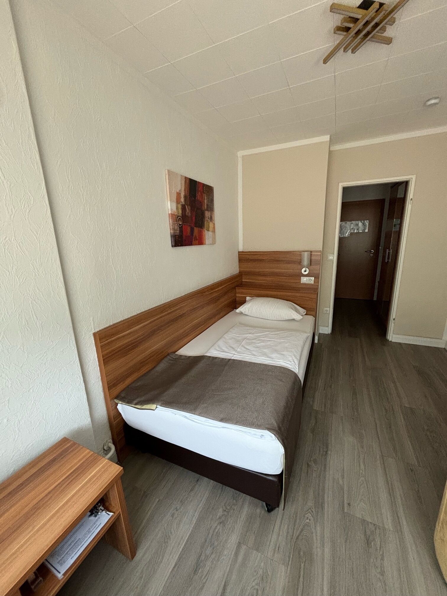 Une chambre à coucher avec une tête de lit en bois, un lit simple, une table de chevet et une petite étagère.