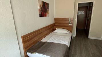 Un dormitorio con cabecera de madera, una cama individual, una mesita de noche y un estante pequeño.