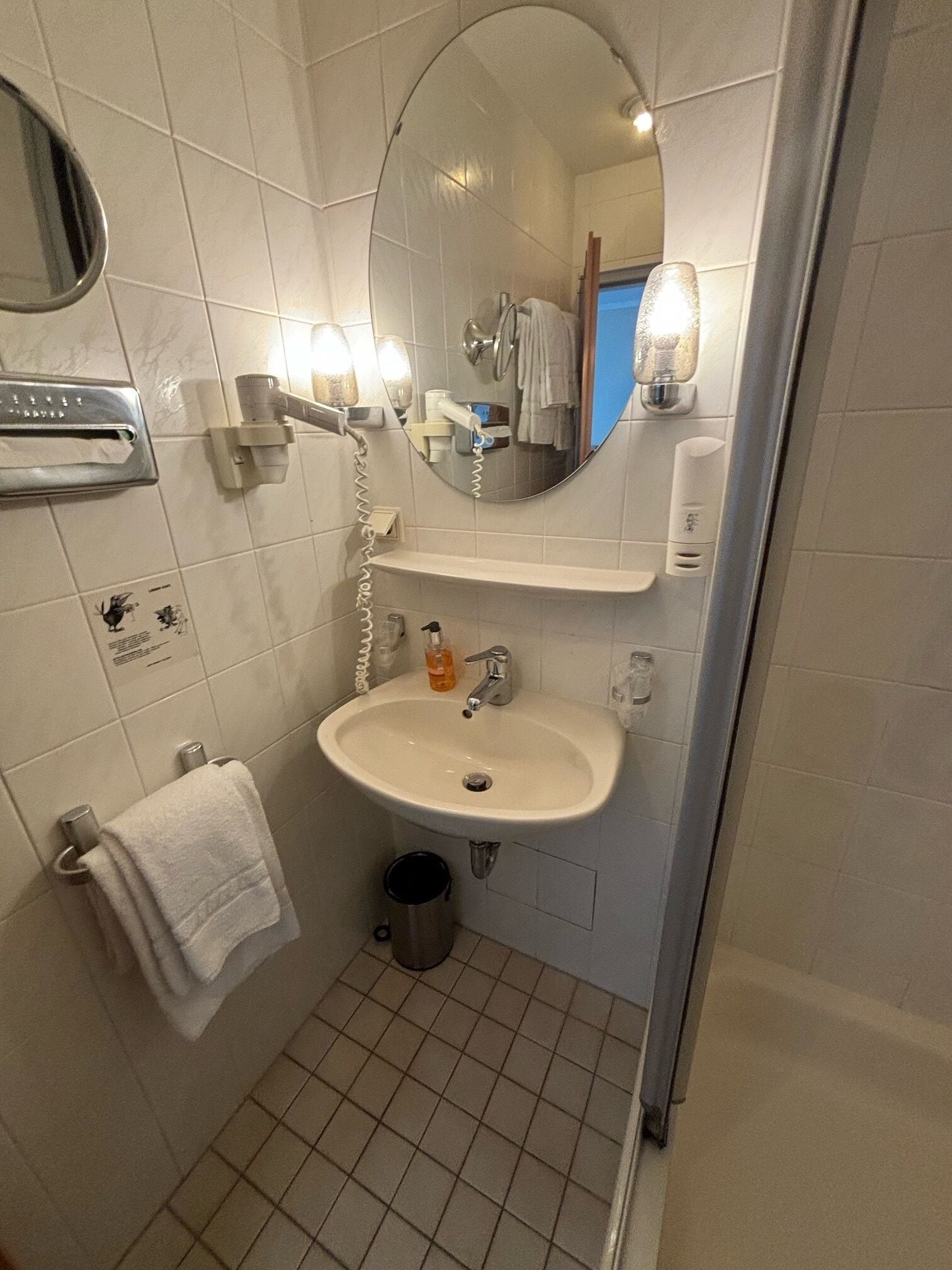 A bathroom with a white sink, a mirror, a towel rack, and a trash bin.