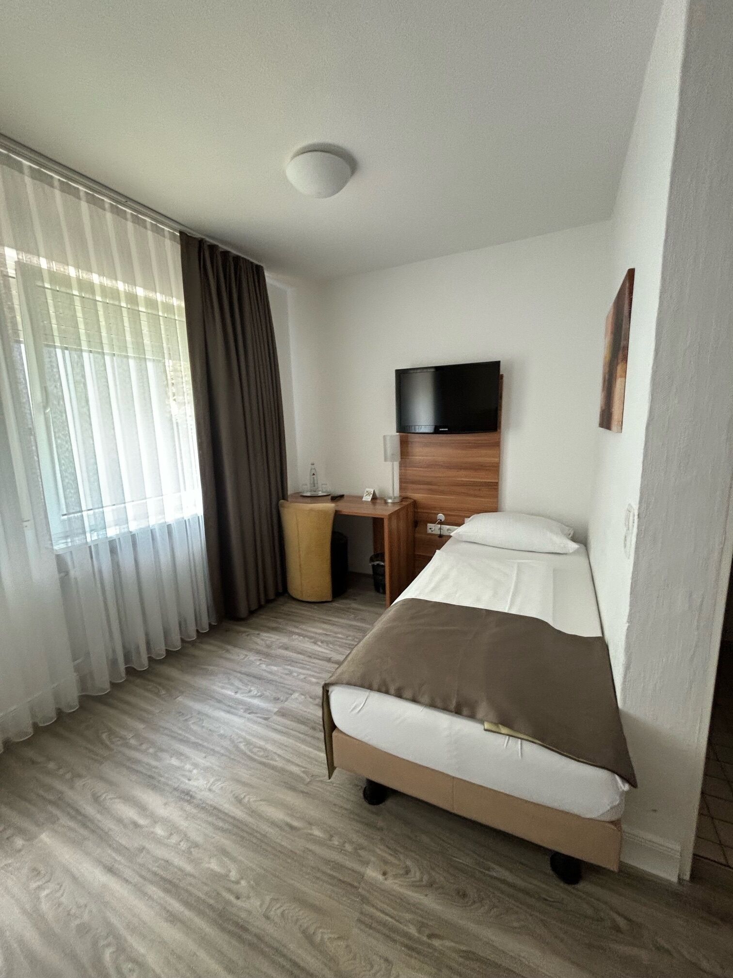 Una habitación de hotel con cama, escritorio, televisión y ventana con cortinas.