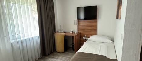 Una habitación de hotel con cama, escritorio, televisión y ventana con cortinas.
