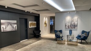 Een modern interieur met een donkere muur, twee blauwe fauteuils, een ronde salontafel en kunstwerk.