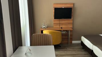 Una camera d'albergo con un letto, una TV montata su un mobile in legno, un tavolino con una sedia e un poggiapiedi giallo.