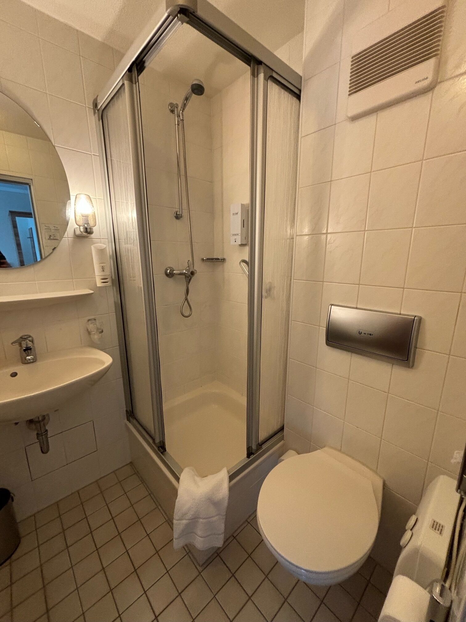 Un baño moderno con ducha de vidrio, lavamanos, inodoro y perchero para toallas.