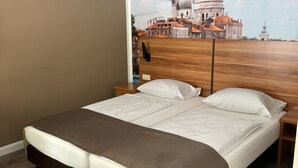 Een tweepersoonsbed met een bruin hoofdbord en wit beddengoed in een kamer met een grote muurschildering van een stadsgezicht.