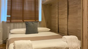 Una cama con cabecera de madera, ropa de cama blanca y una ventana con persianas.