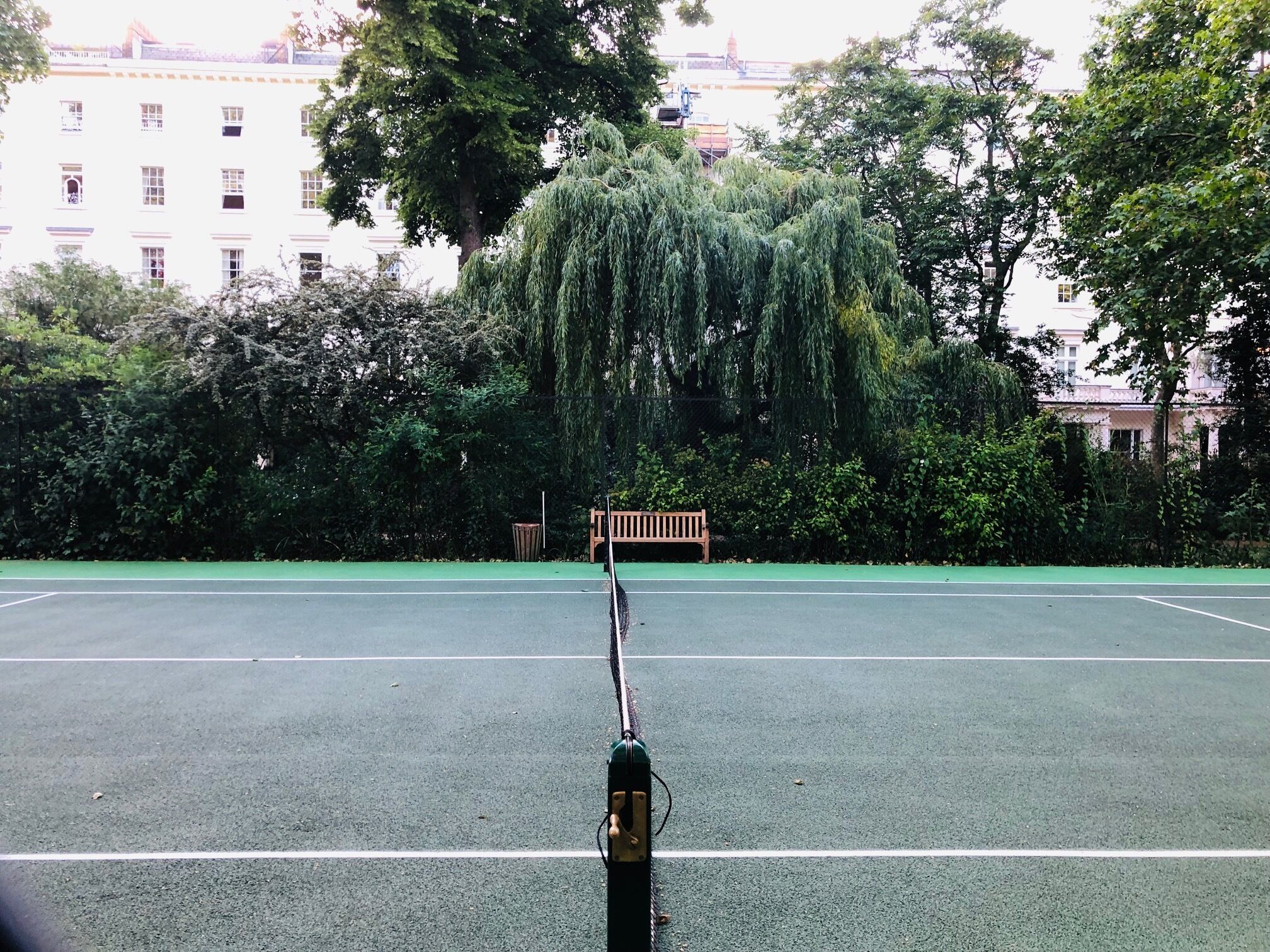 A tennis court with a wooden bench and trees in the background.
