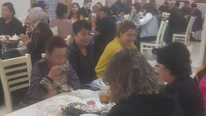 En travl spisesal med borddækning, folk der sidder ned, og forskellige retter samt drikkevarer på bordene.