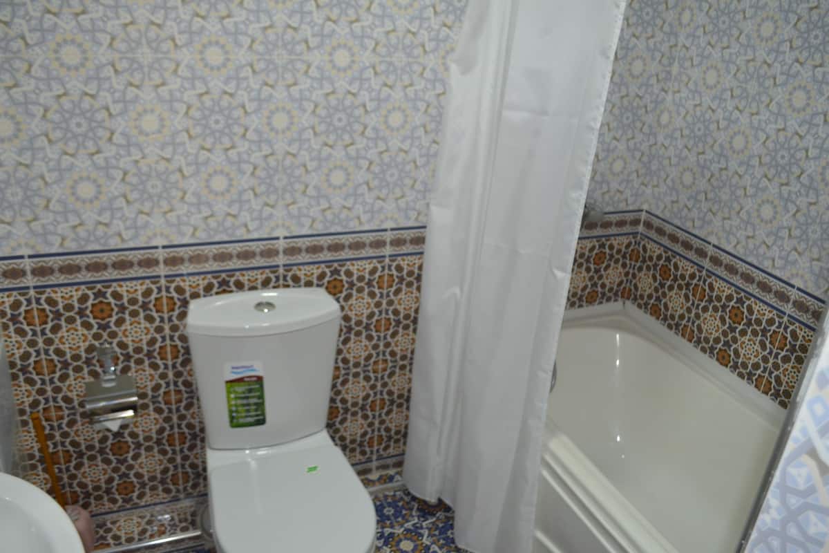 A bathroom with a toilet, bathtub, and patterned tile walls.