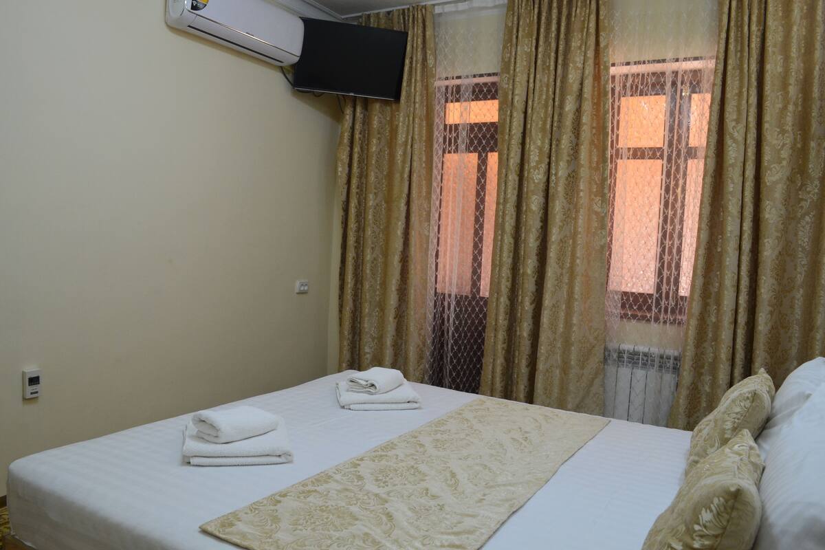 A hotel room with a bed, a TV mounted on the wall, and a window with curtains.