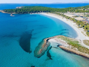 Vista aérea de una zona costera con mar azul cristalino, una playa de arena y un litoral rocoso.