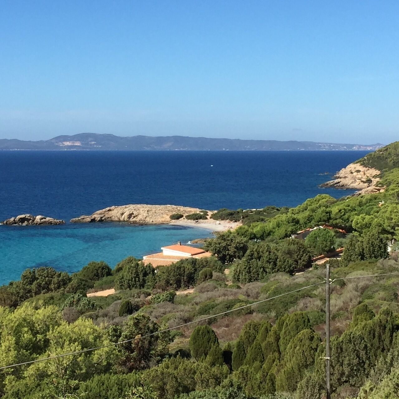 A coastal landscape with a clear view of the sea, rocky outcrops, and dense greenery.