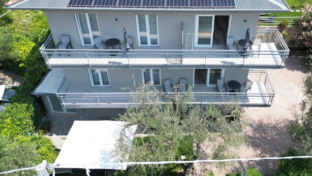 Ein zweistöckiges Haus mit einem geneigten Dach, Solaranlagen und einem Balkon mit Gartenmöbeln.