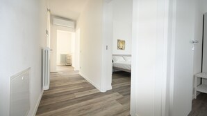 Ein Flur mit einem Heizkörper, einem Heizkörper in der Ferne und einem Bett mit Kopfteil im Hintergrund.