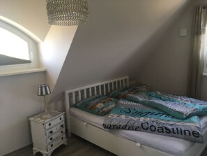 Et soveværelse med en hvid seng, en stribet lampe og en lysekrone.