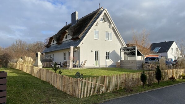 A two-story house with a sloped roof, a fenced yard, and a garage. - Mien Huus 1: An elegant thatched-roof vacation home in Ostseebad-Nienhagen (Nienhagen)