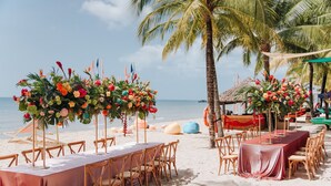 A beachside wedding setup with tables and chairs, floral centerpieces, and palm trees. - MARINA SEASIDE BOUTIQUE HOTEL (Phu Quoc)