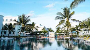 A pool area with lounge chairs, umbrellas, and palm trees.