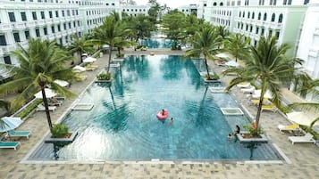 A large indoor swimming pool surrounded by palm trees and white lounge chairs.