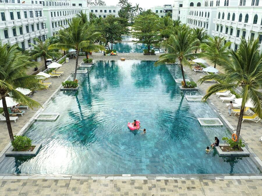 Una grande piscina interna circondata da palme e poltrone da relax bianche.